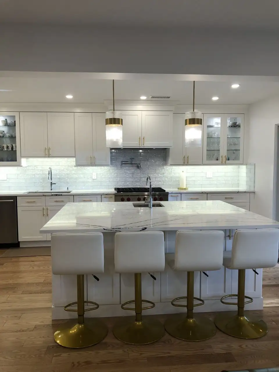 Kitchen cabinets from Westbury showroom DC Kitchen & Bath: white shaker kitchen with brass pulls, glass-front uppers and a veined white island