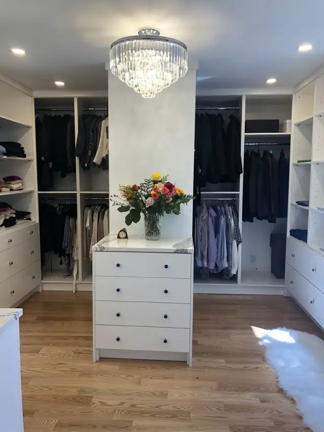 Walk-in closet with white drawer units, open shelving and hanging sections over a wood floor