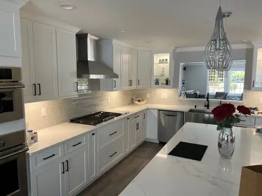 White shaker kitchen with a marble-look island, stainless hood and a glass pendant light
